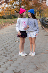 Two girls wearing tennis sweatshirts and cute tennis skirts from love set match tennis wear