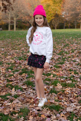 Young girl wearing white tennis sweatshirt and black tennis skirt with hearts printed on it from Love Set Match girls tennis wear