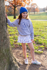 Girl standing by tree wearing gray tennis sweatshirt and tennis skirt from Love Set Match